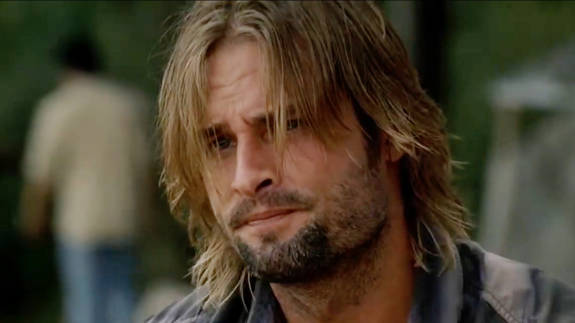 Sawyer looks out to the ocean as his bangs fall in front of his face. He has a look of sadness. 