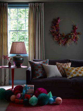 Paper bauble decorations in jewel tones on the floor next to a velvet sofa in a dark gray living room