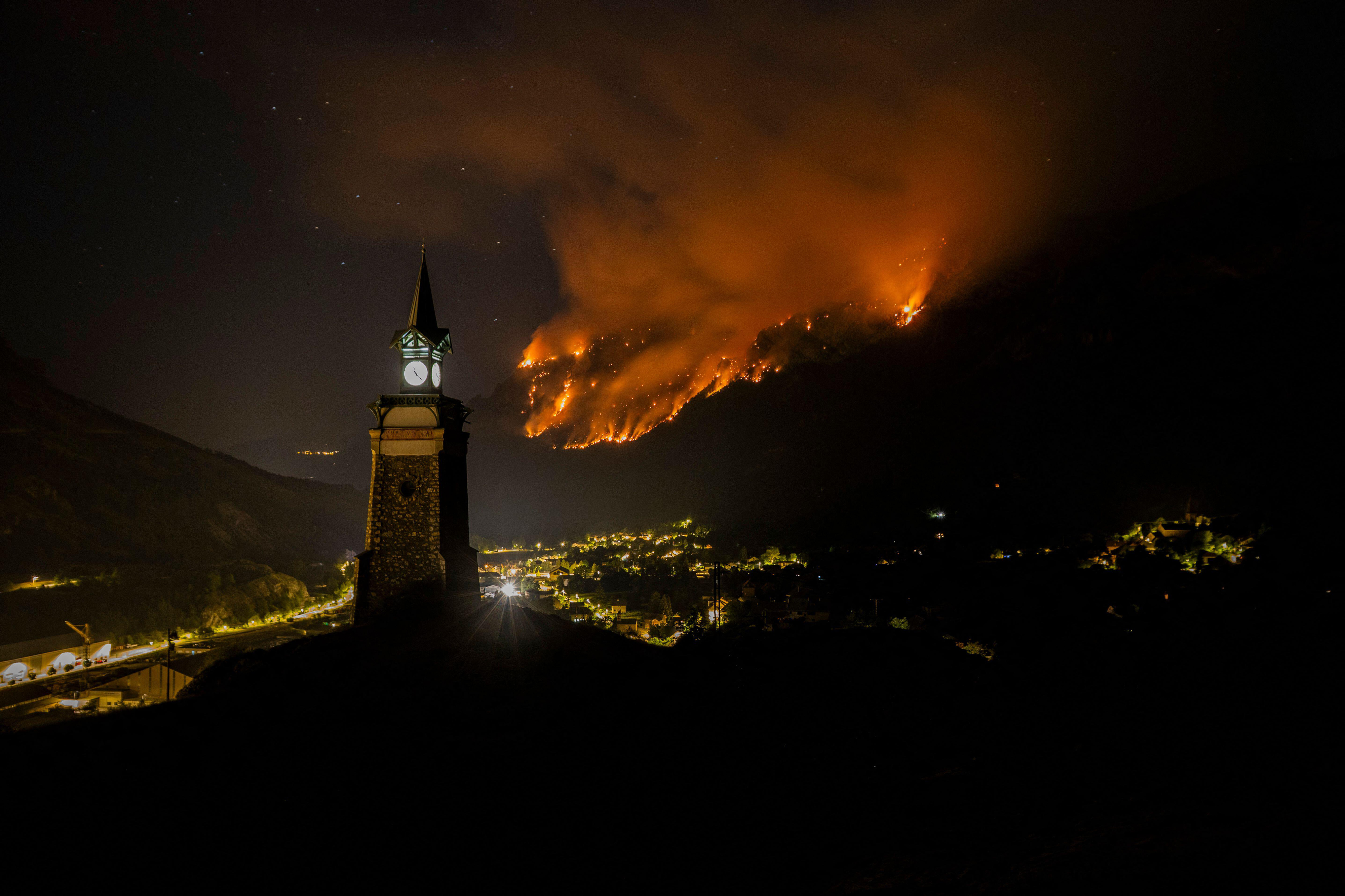 The Horloge des Hermes stands in the foreground as a major wildfire burns across the mountains overlooking L Argentiere la Bessee, a long fire front advances through the forest during the night as extreme heat and prolonged drought fuel one of the most severe wildfire events of the summer in the French Alps, Hautes Alpes, France, July 20, 2026. Photo by Thibaut Durand/ABACAPRESS.COM