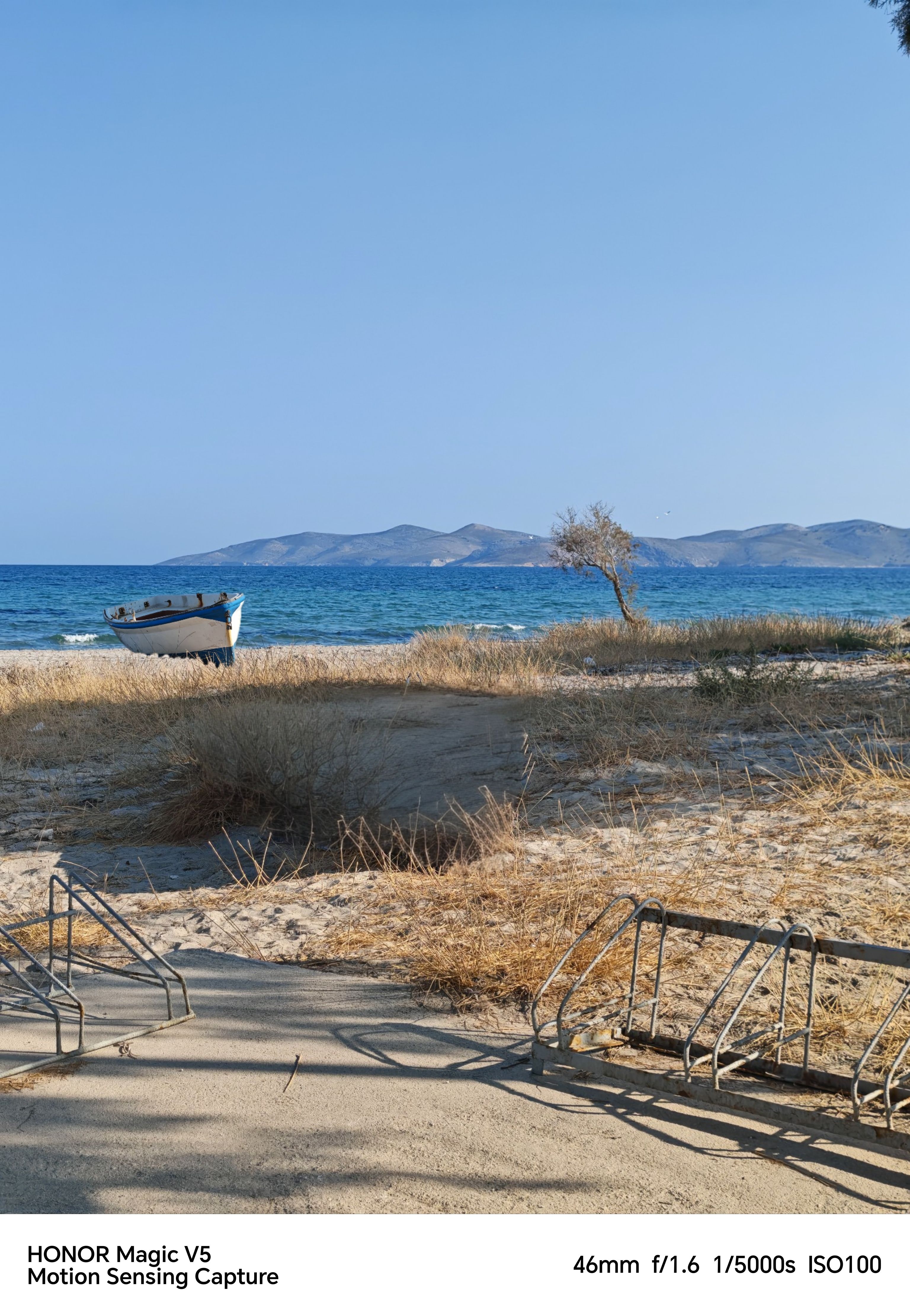 Sandy Beach with a boat on the edge of the blue Ocean in front of a mountain and blue sky
