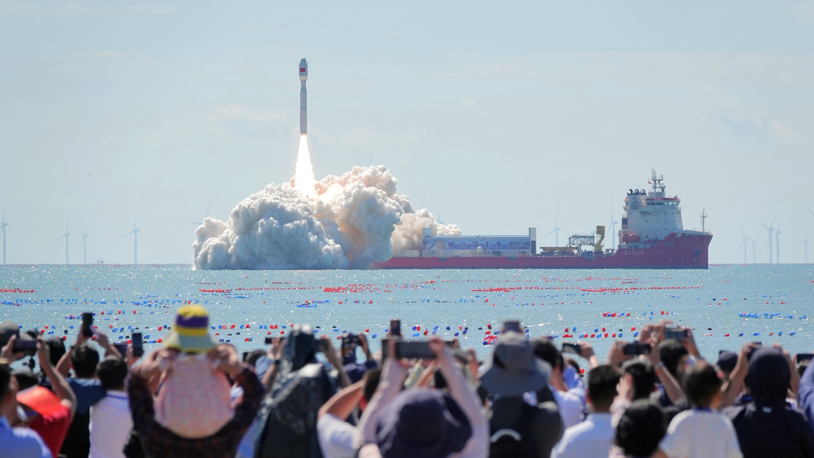 A photo of a rocket launch at sea in China with hundreds of people watching from the shore