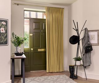 white hallway with green front door and yellow curtain on pole to cover it, black coat stand and small console table