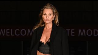 Kate Moss is pictured wearing a black dress and coat, with her hair swept back whilst arriving at the Gucci Cruise 2025 Fashion Show at Tate Modern on May 13, 2024 in London, England.