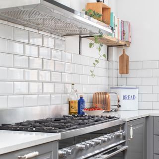 White tiled corner of a kitchen with grey cabinets and a gas hob