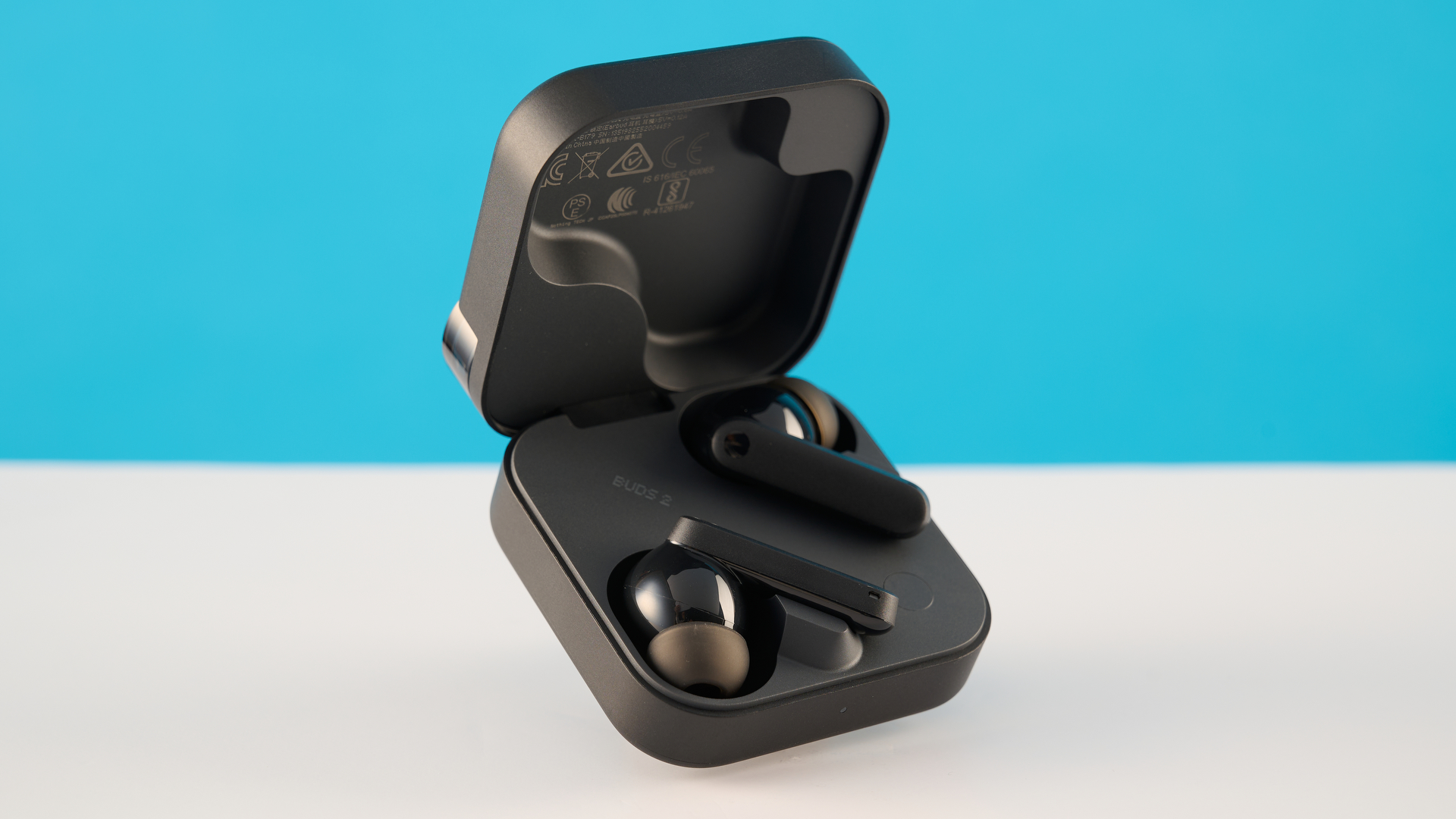 CMF Buds 2 in Dark Gray photographones on a gray table in front of a blue background