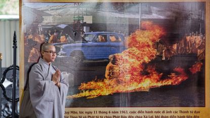 A Buddhist monk stands next to a banner with a picture of monk Thich Quang Duc, who set himself on fire on a busy Saigon street corner in 1963