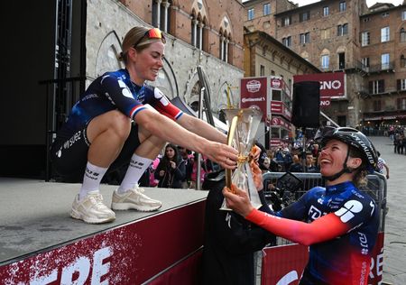 Demi Vollering celebrates victory at the 2025 Strade Bianche, handing her trophy to teammate Marie Le Net