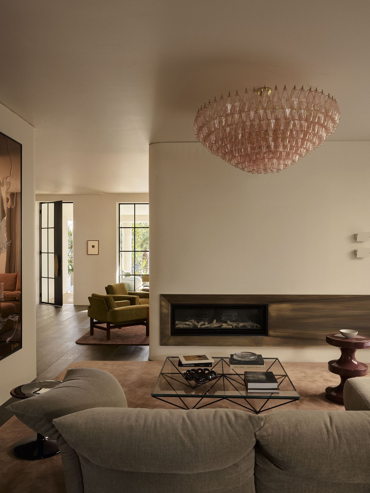 Living area in Smac Studio's renovated Art Deco home in Woollahra, Sydney, featuring a curved fireplace wall, vintage pink Murano glass chandelier and interconnected open-plan living spaces.