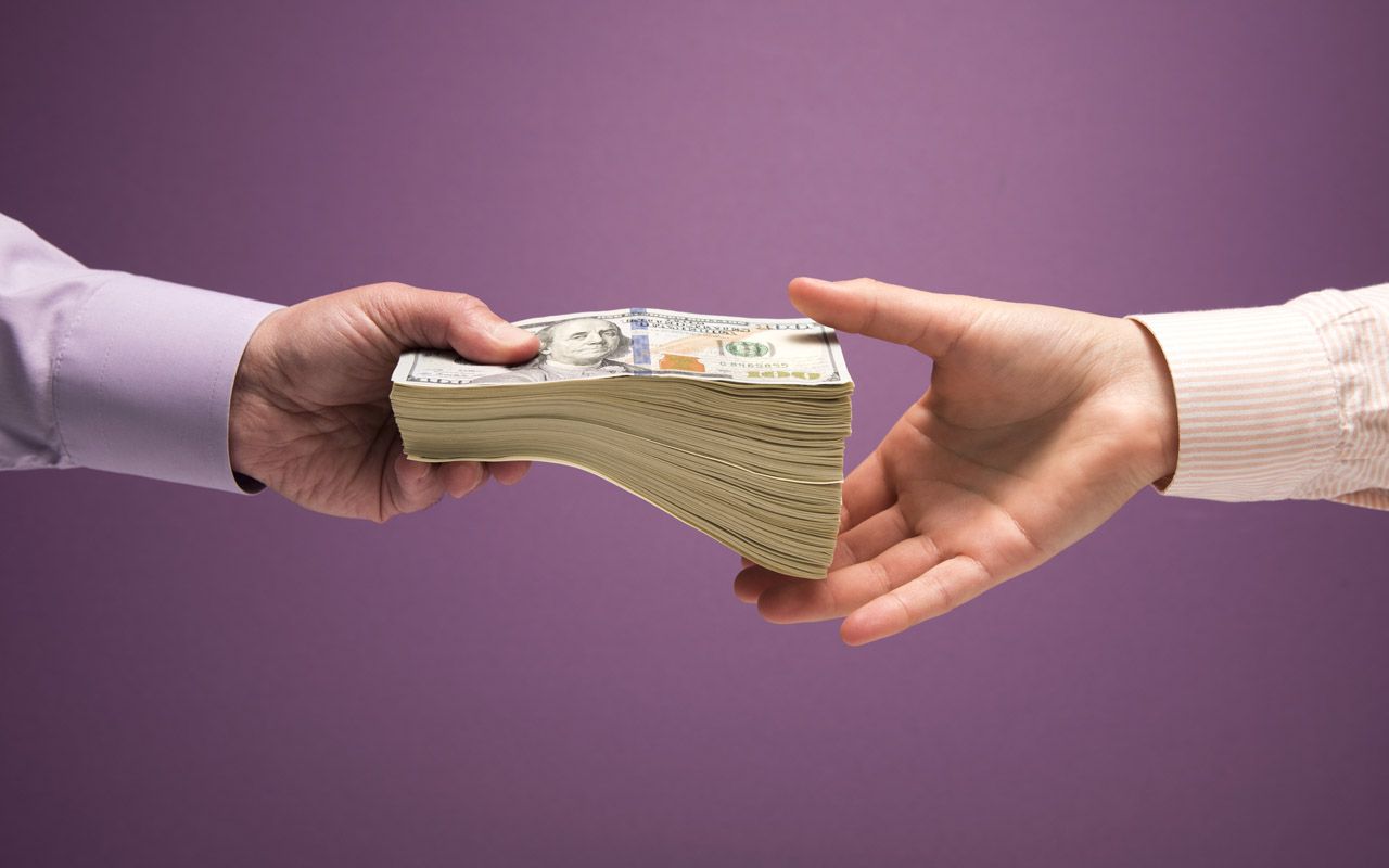 One man and one woman&amp;#039;s hands handing off large stack of US 100 bills, purple background