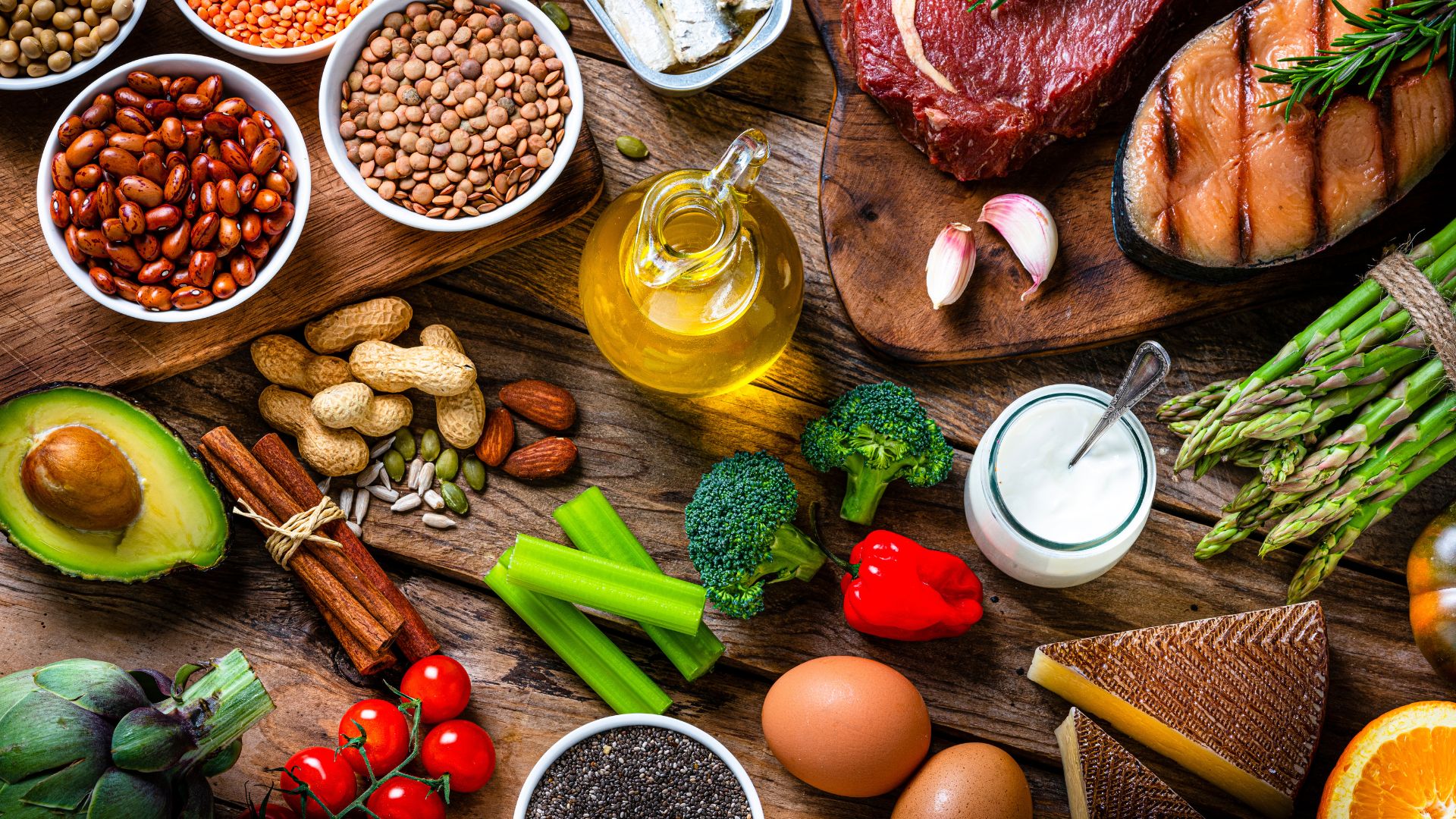 Whole foods, including beans and lentils, meat and sardines, vegetables and garlic sitting on wooden board
