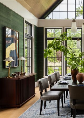 A dining room with large windows, a buffet, framed art, pendant lighting and a set of vases with stems