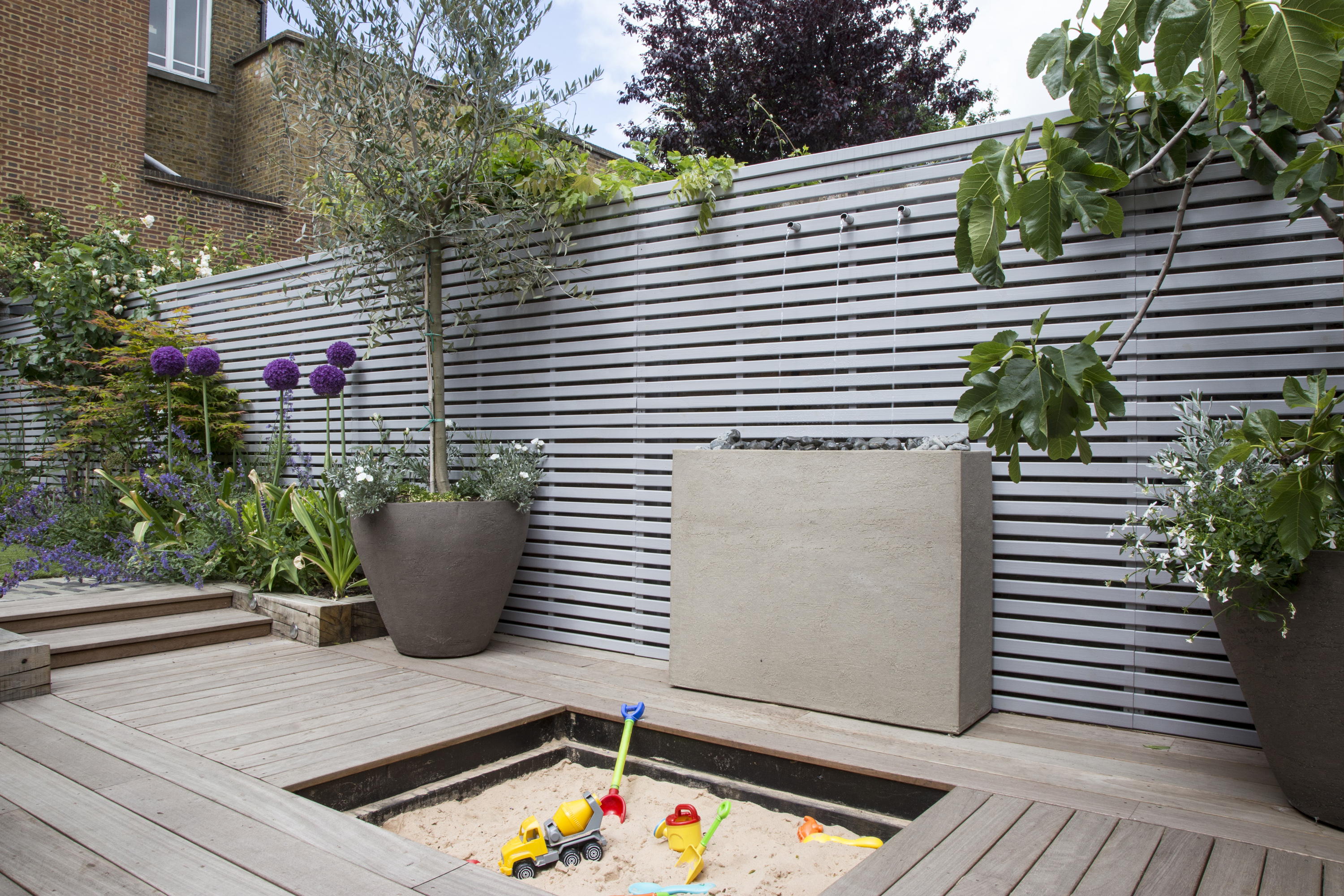 modern grey fencing teamed with a decked terrace and built-in sandpit