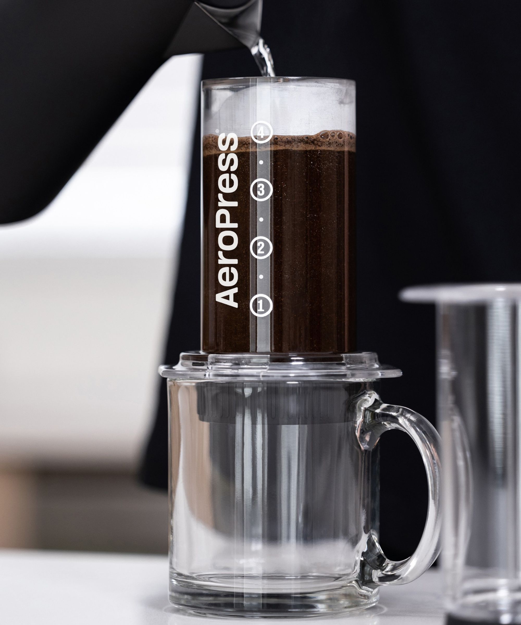A clear AeroPress brewing coffee over a clear cup