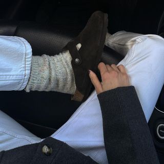 Influencer wearing suede Birkenstock clogs with white jeans and black cardigan.