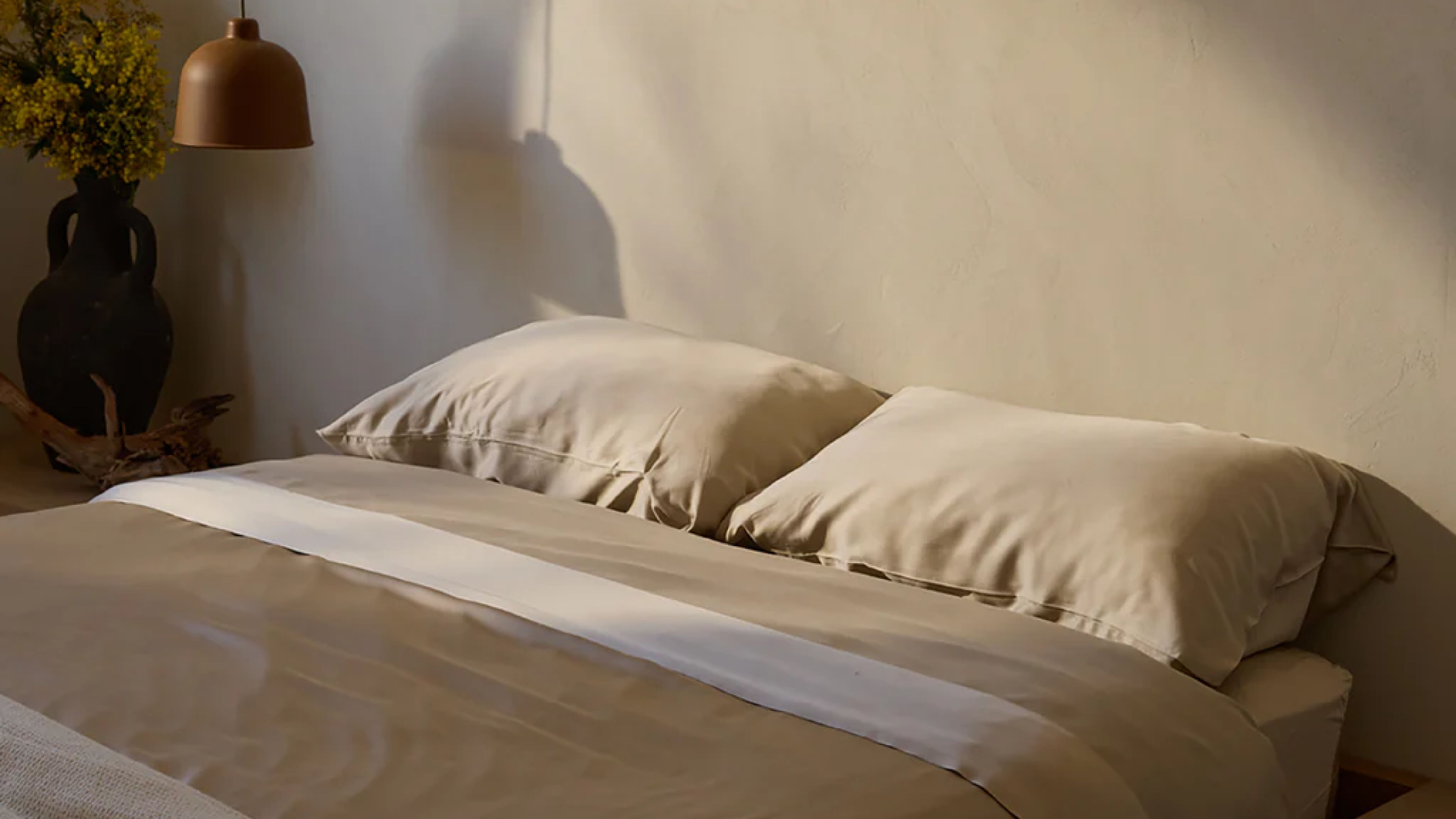 Cozy Earth bamboo viscose duvet set pictured in a similarly hued beige bedroom with a sculputral black vase and dome shade pendant light