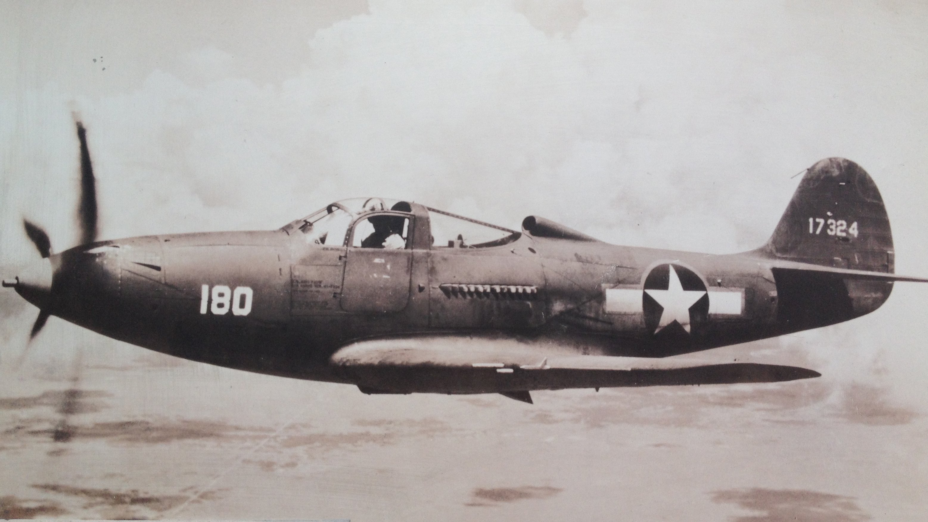 We see a black-and-white photo of a P-39 Bell Airacobra flying in the air.