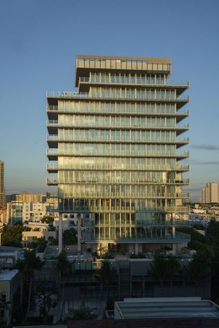 Front view of Rene Gonzalez’s crystalline building. High-rise building with glass banisters and palm trees in front of it.