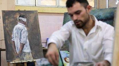 A Syrian artist works on portraits of people imprisoned by the former dictator, Bashar al-Assad, during his trial in absentia