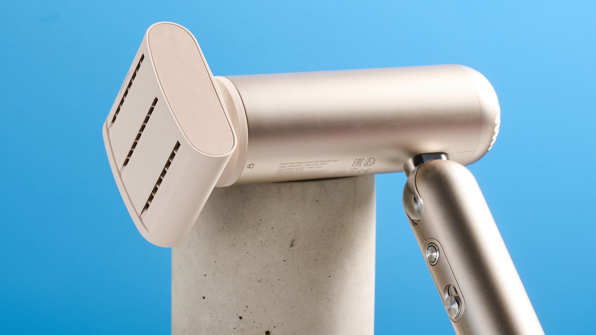 The Dreame Pocket Neo in gold with anti-frizz attachment photographed in front of a blue background.