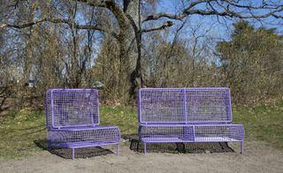 Two purple benches are made from wire, that look like furniture. One is smaller, like an armchair, and the other one is like a two-seat sofa.