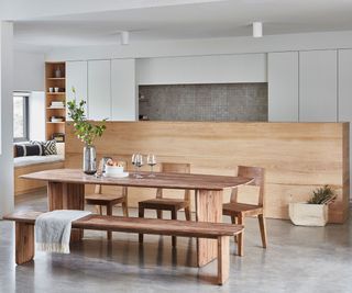 wooden dining table and chairs in front of a kitchen area decorated with wood and white finishes and grey tiles