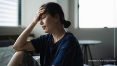 Woman holding head in hand in bedroom, dealing with perimenopause fatigue