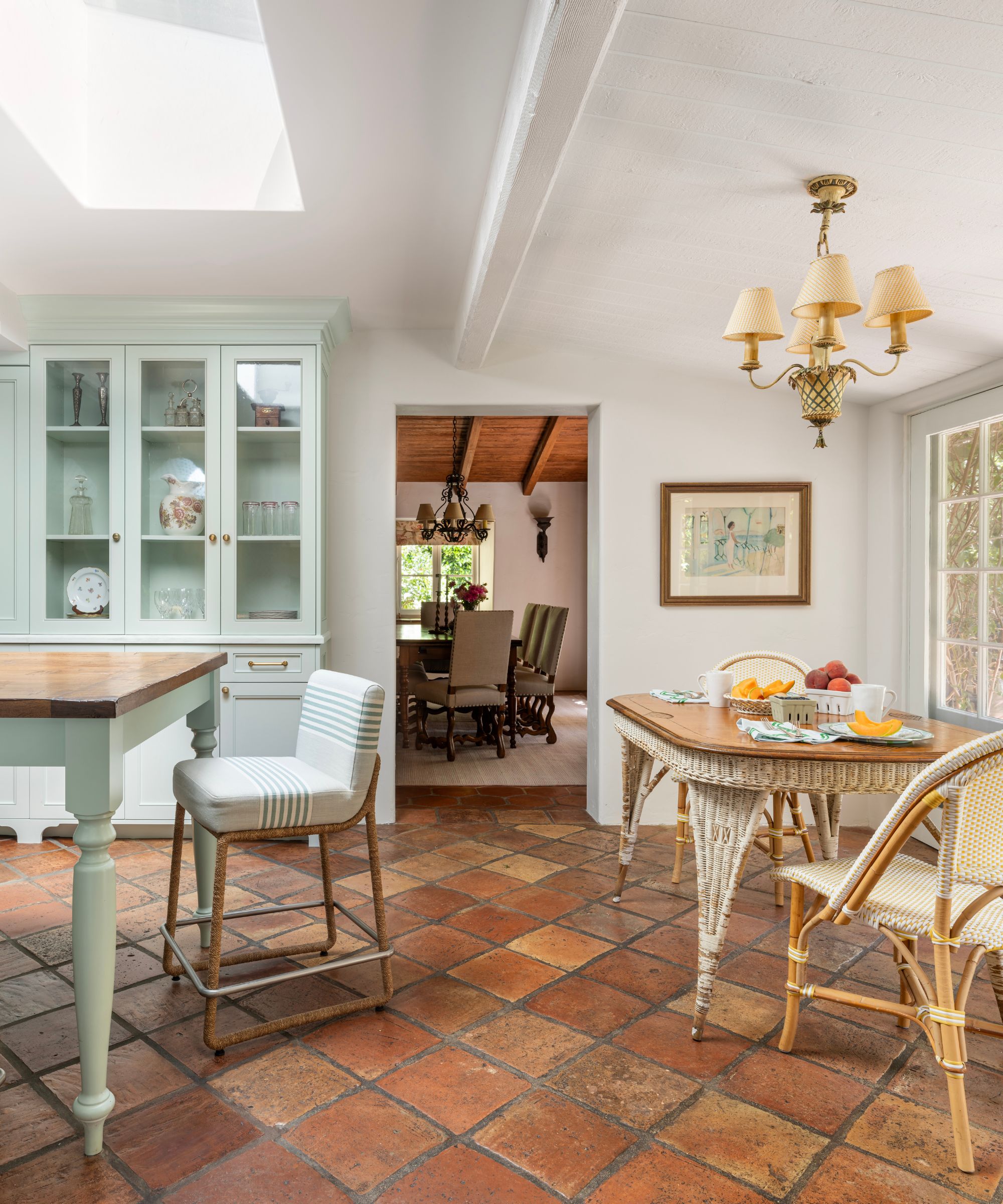 An open-plan kitchen with terracotta flooring, blue/green cabinetry, and a vintage dining table and chairs