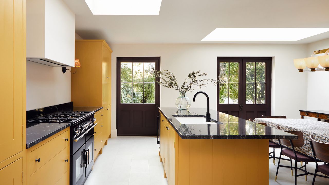 kitchen island color ideas, yellow and white kitchen with black crittall doors, yellow kitchen island, black countertops, skylights, white flooring 