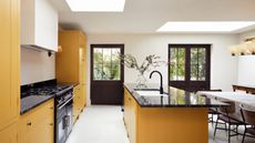 kitchen island color ideas, yellow and white kitchen with black crittall doors, yellow kitchen island, black countertops, skylights, white flooring 