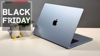 MacBook Air in sky blue on a white desk with a plant and a Black Friday sign.