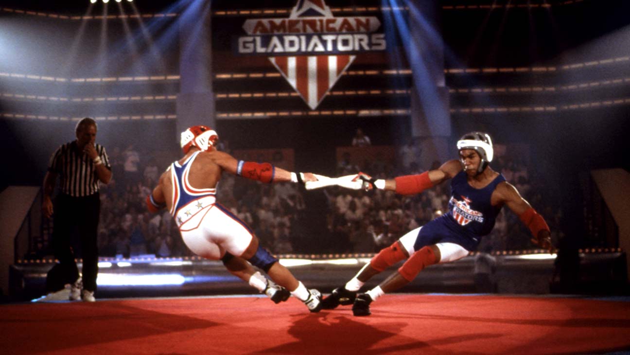 A still from American Gladiators showing two athletes in costume and helmets doing a kind of tug of war in an arena