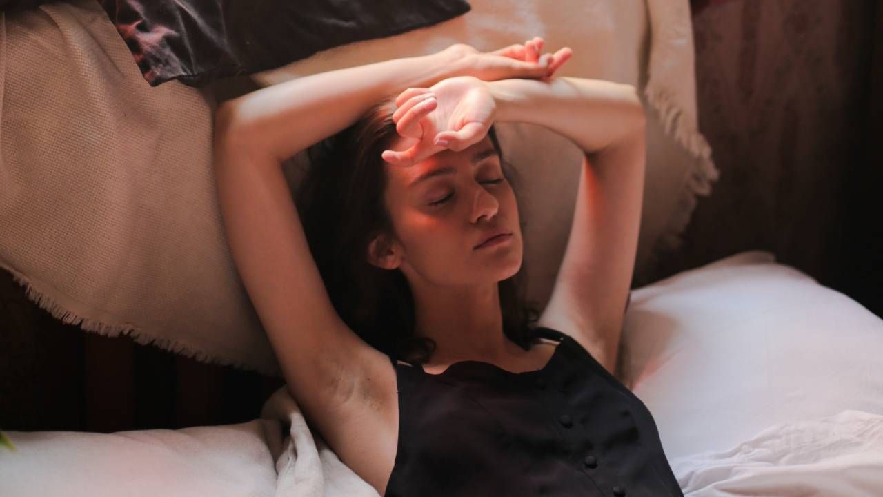 Woman sleeping in bed with her arms above her head, sleep &amp; wellness tips