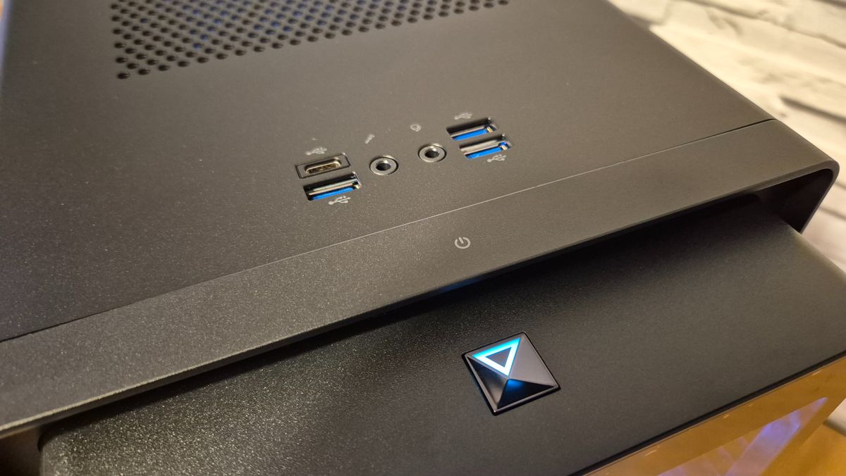 A close-up of the buttons and ports on the front of an Acer Predator Orion 5000 gaming PC as it sits on top of a wooden surface in front of a white brick effect wall