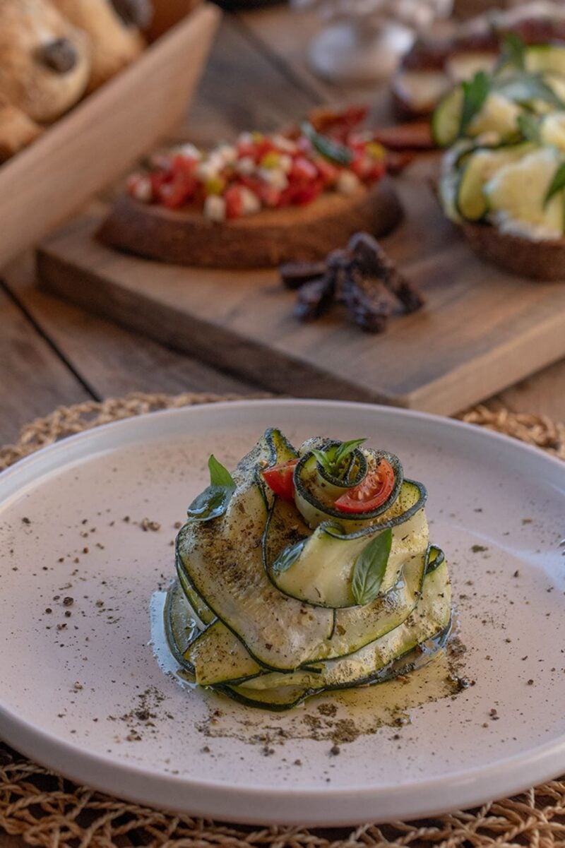 A beautifully plated grilled courgette plate presented as a rose, topped with basil and tomatoes and sprinkled in oregano.