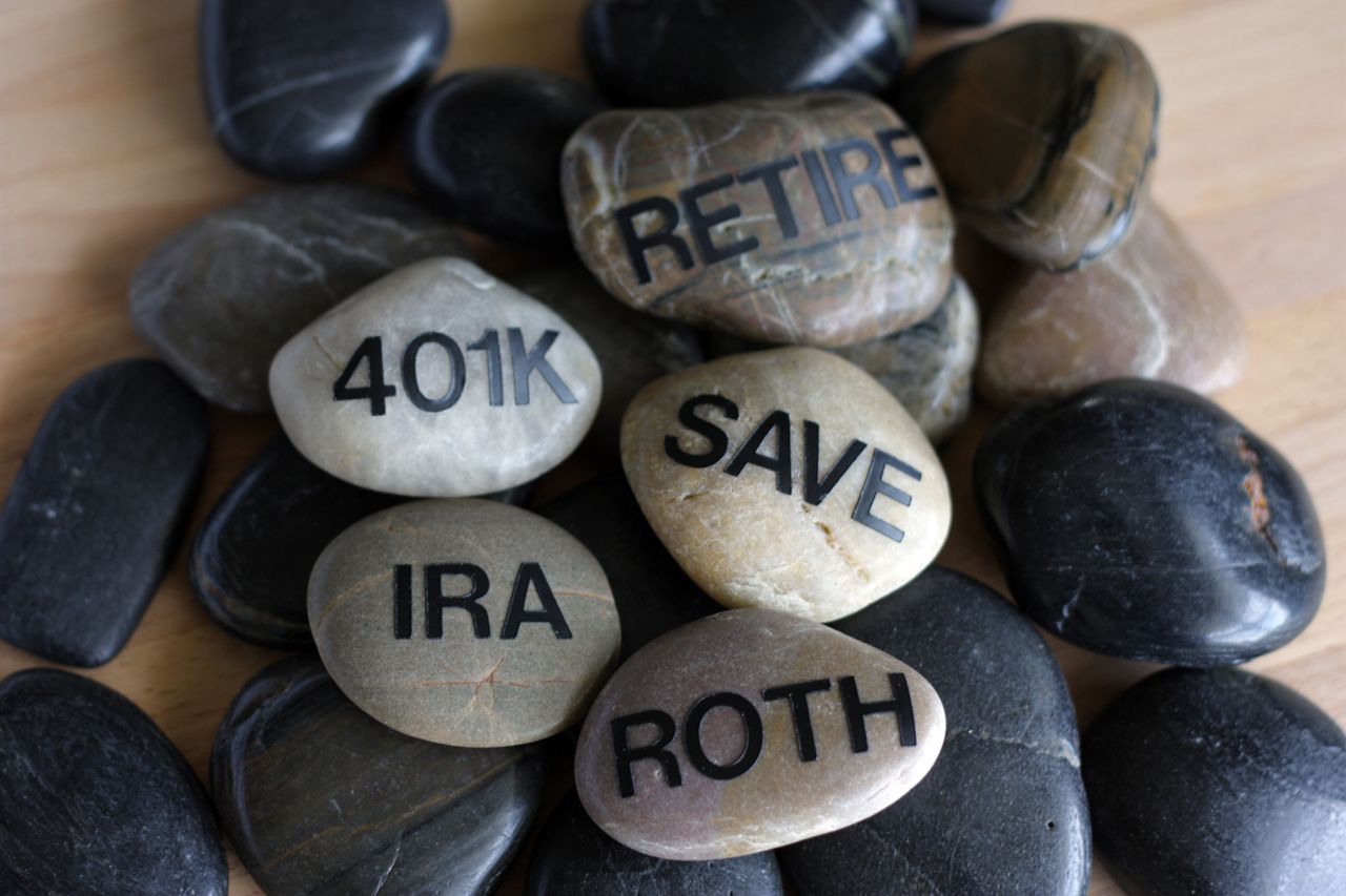 Smooth rocks with the words retire, 401K, IRA, roth and save on them arranged in a zen-like way.