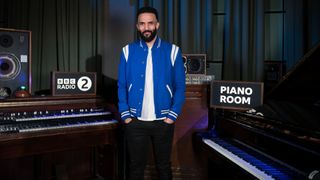 Craig David in a blue varsity jacket poses in the BBC Radio 2 Piano Room