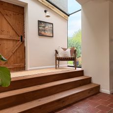 Three wooden steps leading from terracotta floored area to hallway with armchair