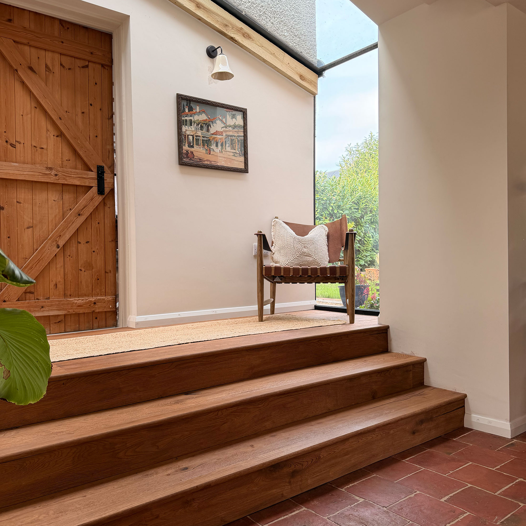 Three wooden steps leading from terracotta floored area to hallway with armchair