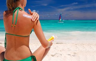 A woman on the beach applying sunscreen.