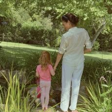 Princess Lilibet holding Meghan Markle's hand in front of trees