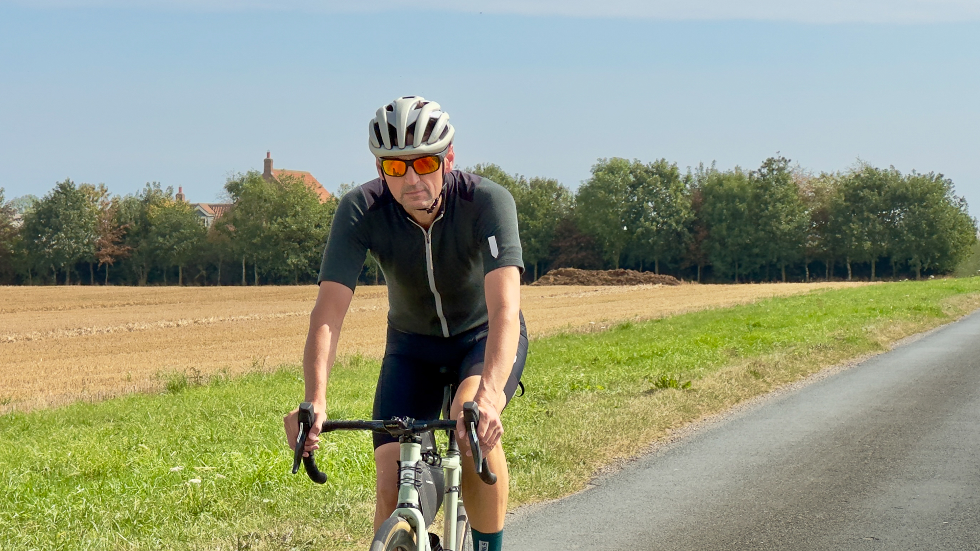 man wearing a dark green jersey and beige helmet riding towards the camera