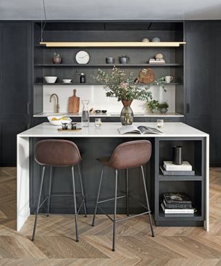 Kitchen with wooden flooring, black and cream fitted units, bar stools by the breakfast bar, high ceilings and coving.