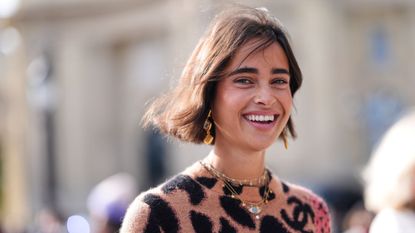 A smiling woman wears dark brown black leopard pattern/print red floral pattern/print sweater with short brown hair 