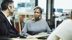 An older woman talks with a co-worker while sitting at a conference room table.