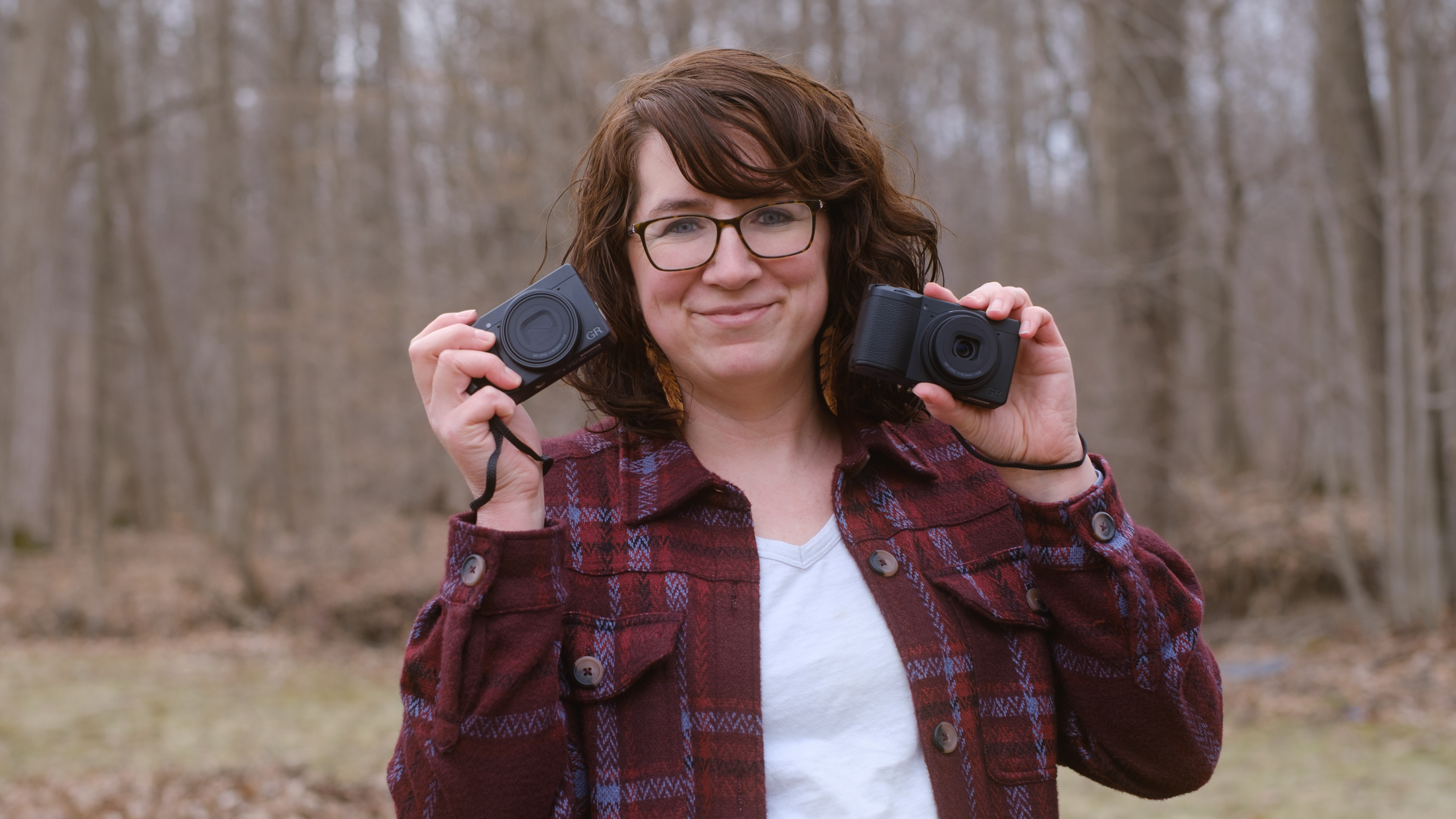 A photographer holds the Ricoh GR IV HDF in one hand and the Ricoh GR IV Monochrome in the other