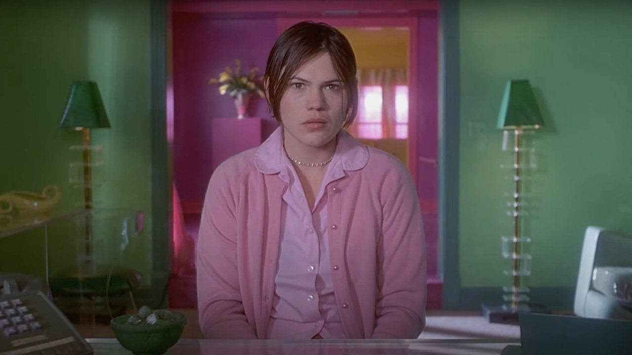 Clea DuVall in But I'm a Cheerleader sitting at the camp director's desk staring blankly at the camera.