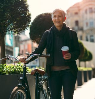 woman walks beside bike with a coffee in hand