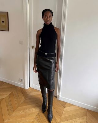 @sylviemus_ wearing knee-high boots with a leather skirt and halterneck top