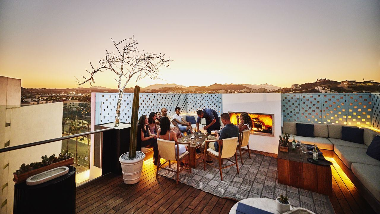 A wealthy family enjoys dinner on a rooftop at sunset.