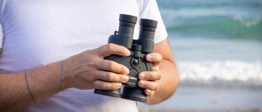 A person holding the Canon 12x36 IS binoculars with the sea in the background.